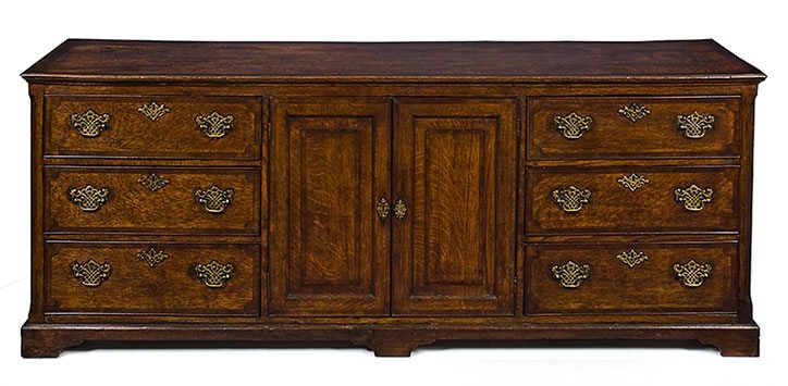 An outstanding 18th Century English oak dresser base.  The well patinated magogany cross banded top above a pair of centre panelled doors, flanked by two banks of graduated drawers, all cross banded. With later but appropriate brasswork, resting on shaped bracket feet. Good overall colour and patination 1770 - 1800 - Courtesy Allpress Anttiques, Malvern