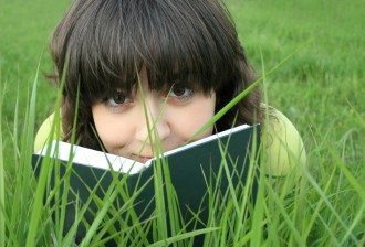 Pretty girl on the grass looking over the book